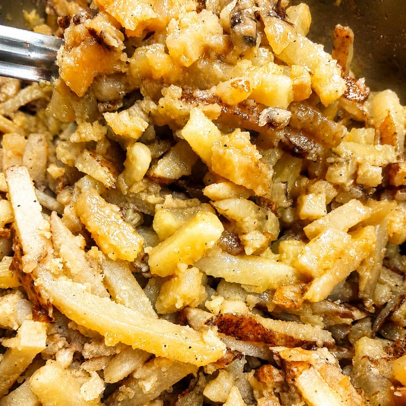 Close-up of golden-brown home fries with crispy edges and seasoning, being stirred with a fork.