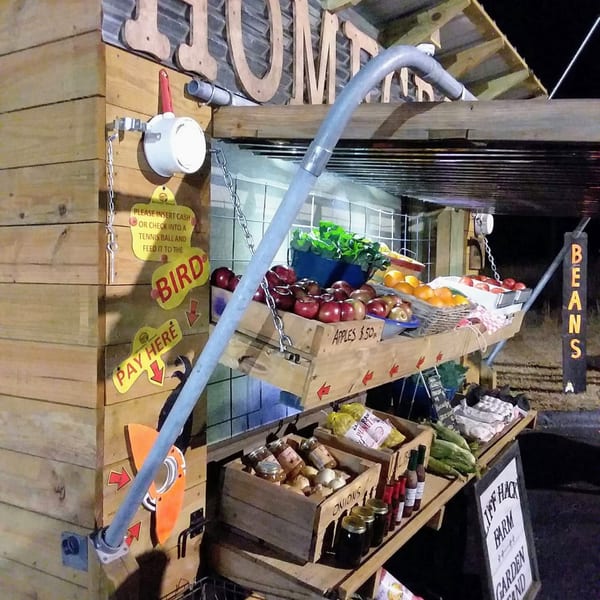 A rustic farm stand at night, displaying fresh apples, onions, and other produce in wooden crates.