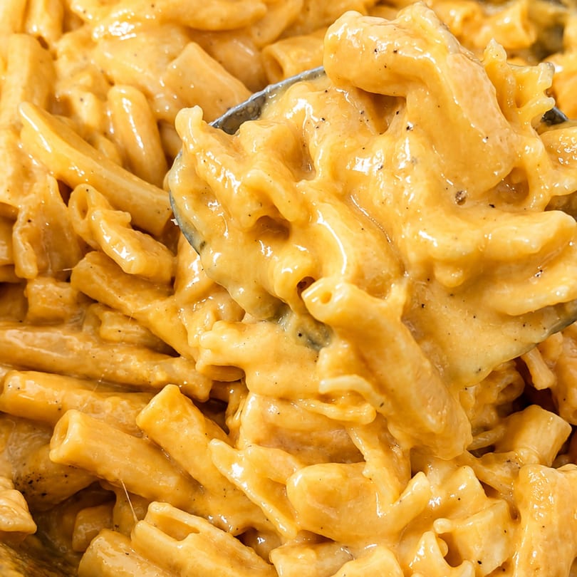 Close-up of creamy mac and cheese with black pepper, being scooped with a spoon.