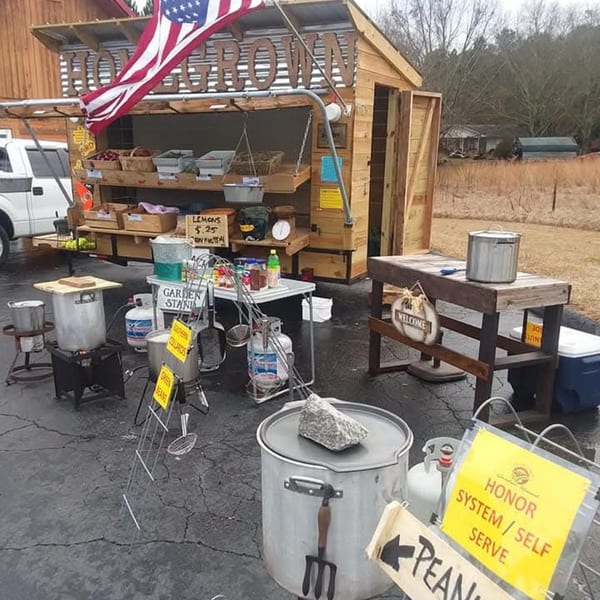 A rustic roadside stand with a "Home Grown" sign, selling produce and prepared foods.