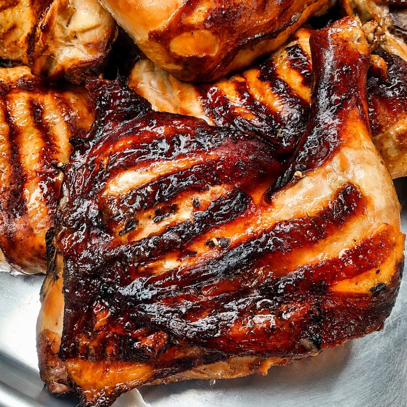 Close-up of several pieces of grilled chicken, glistening with a dark, savory glaze.
