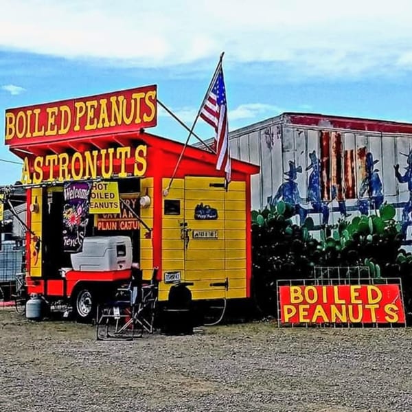 A red and yellow food truck with "BOILED PEANUTS" and "ASTRONUTS" signs, an American flag, and cacti.