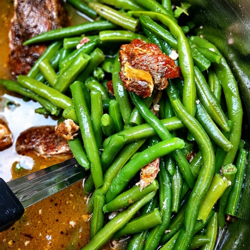 Close-up of green beans and meat in a savory sauce, with a serving spoon.
