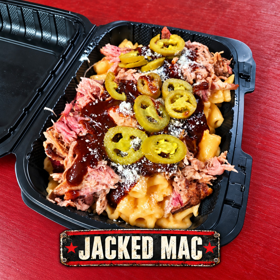Loaded Jacked Mac container with macaroni and cheese, pulled meat, barbecue sauce, jalapeños, and coleslaw on a red table.