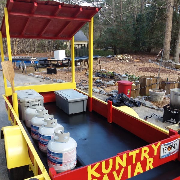 A red and yellow food cart with propane tanks and storage containers, labeled "KUNTRY CAVIAR".